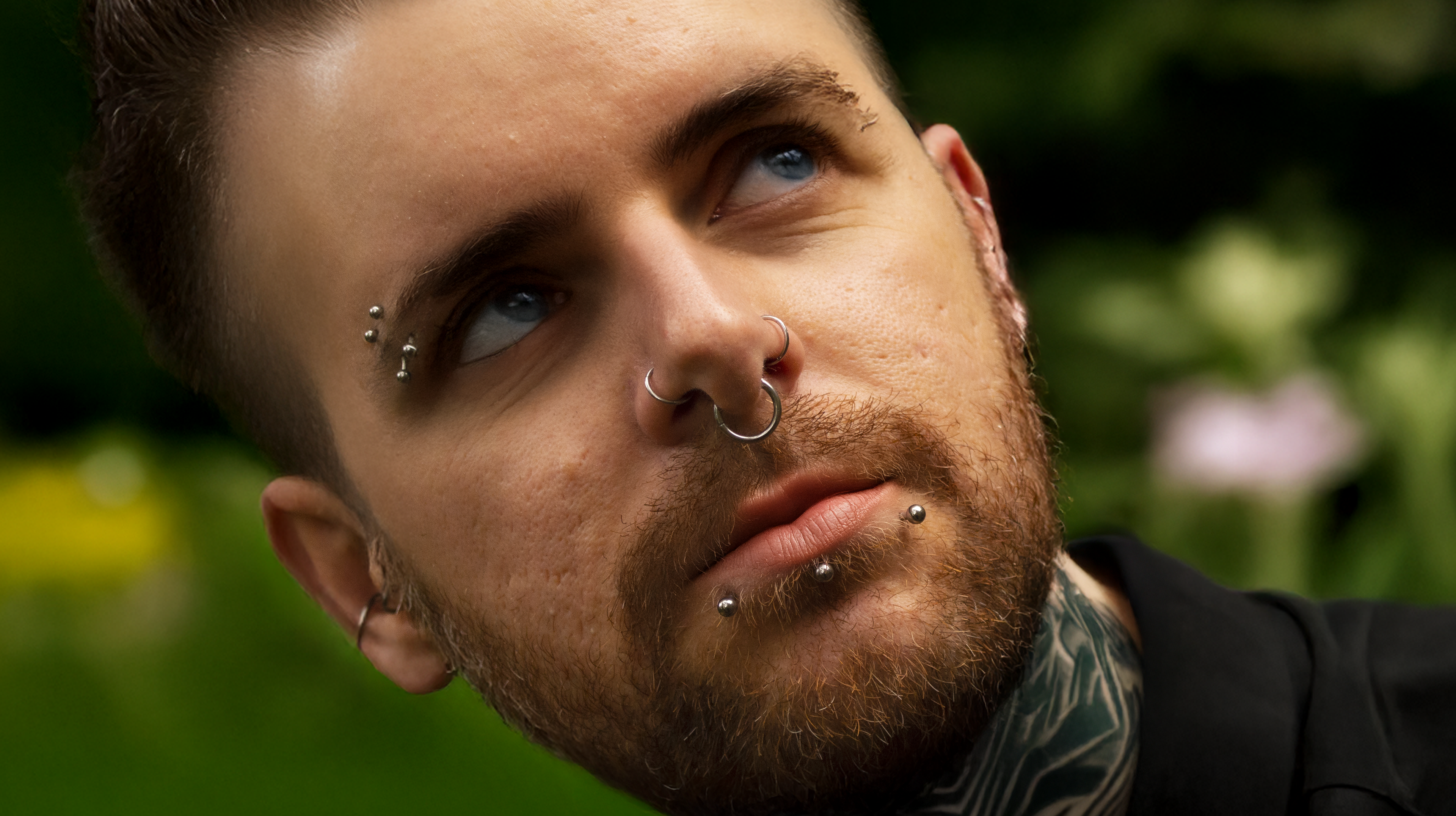 man with eyebrow, nose and lip piercings and neck tattoos outside